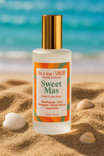Bottle of 'Sweet Mas' room and linen spray on a sandy beach with ocean in the background